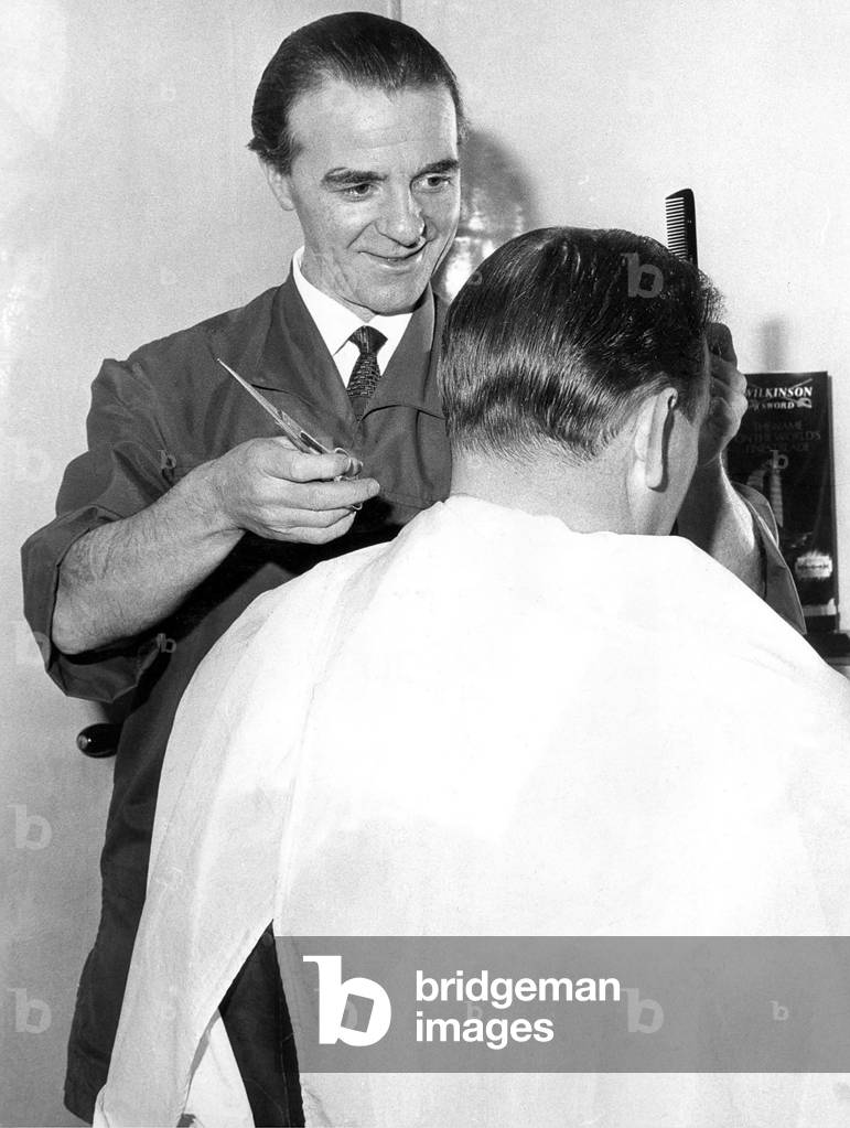 An old fashioned barber cutting a mans hair in February 1966 (b/w photo)