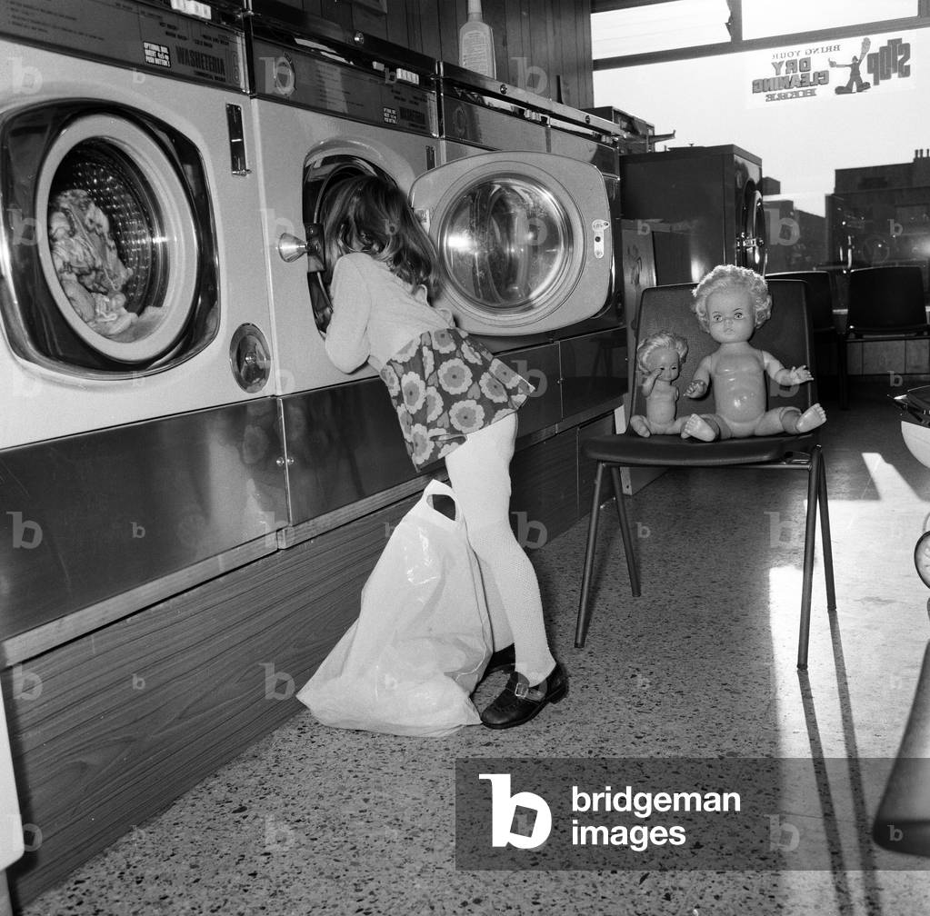 Four year old Tracy Smythe of High Barnet, likes to live in a make believe world. One of her favourite games is to play 'Mum in the Launderette'. She 'washes' her dolls clothes in the empty machine at 'Rub A Tub' launderette owned my Mr Jim Rose. 10th December 1972 (b/w photo)