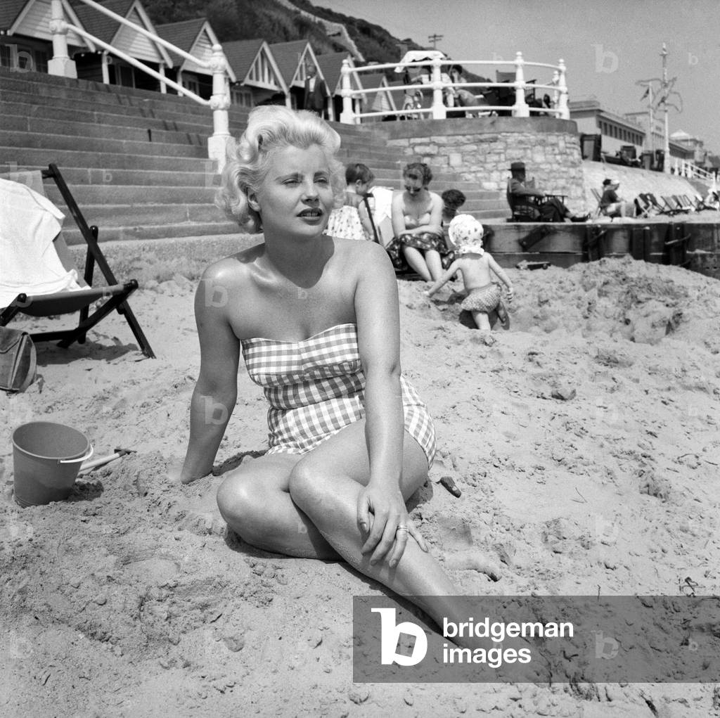 A blonde girl on the beach at Bournemouth wearing a checkered patterned swimsuit
June 1960