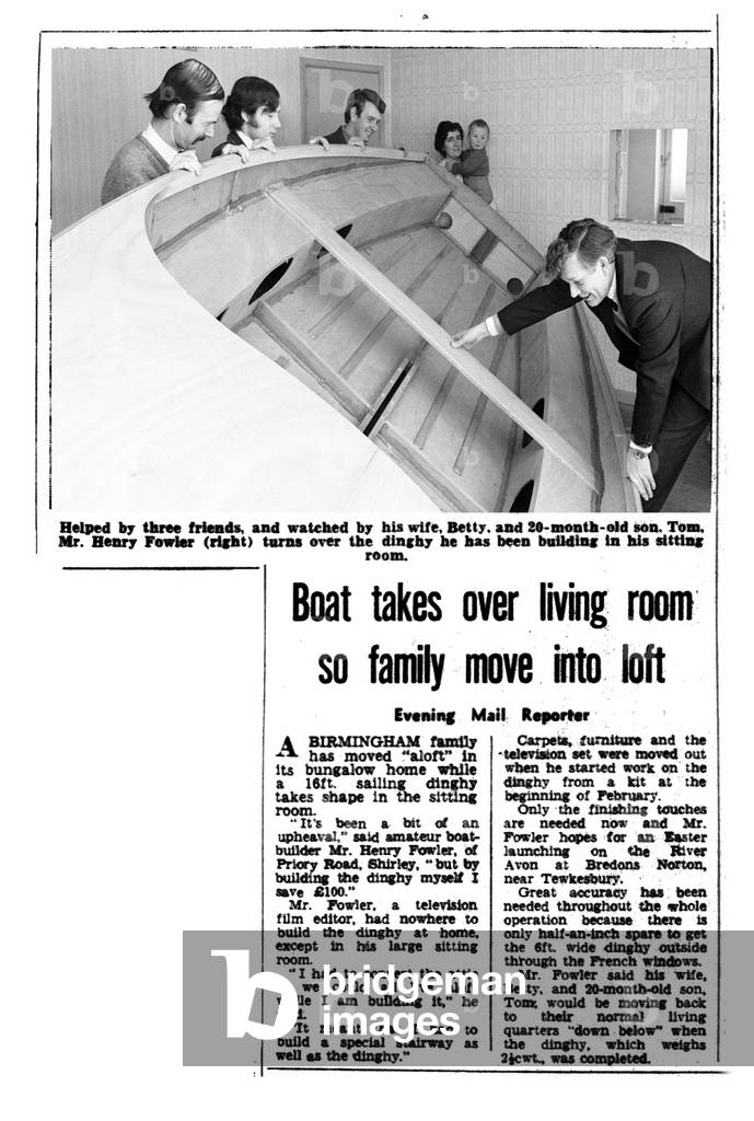 Helped by three friends and watched by his wife Betty and 20 month old son Tom, Mr Henry Fowler (right) turns the dinghy he has been building in his sitting room 11th March 1970 (b/w photo)