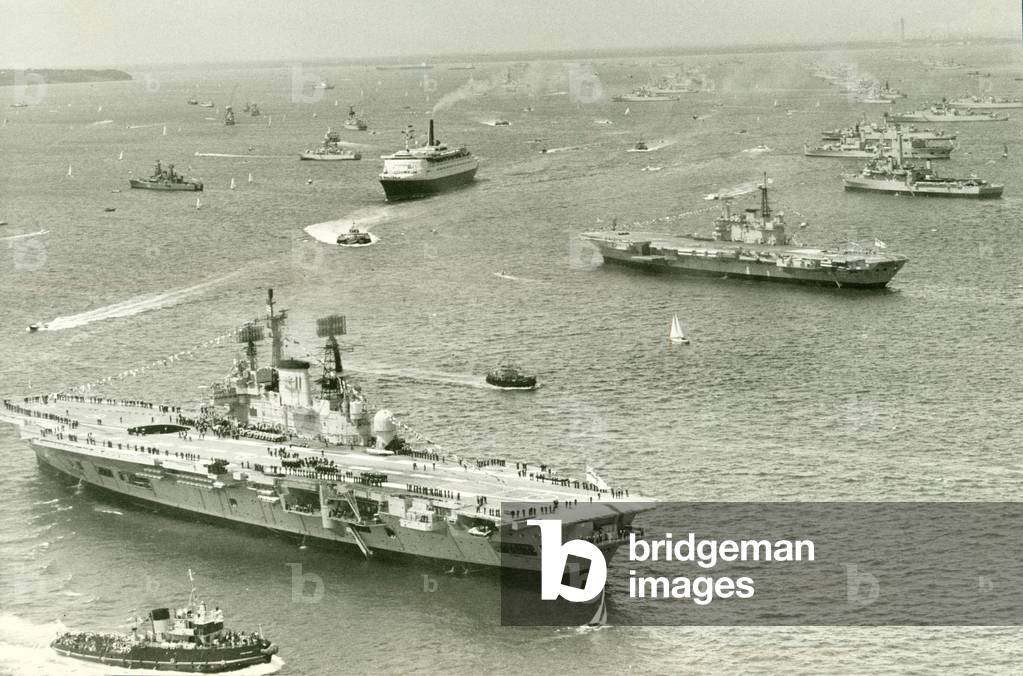 The Cunard liner QEII cruises through the fleet of Royal Navy ships gather at Spithead for the Queens silver jubilee review In the foreground the Aircraft Carriers HMS Ark Royal and HMS Hermes. June 1977 (photo)