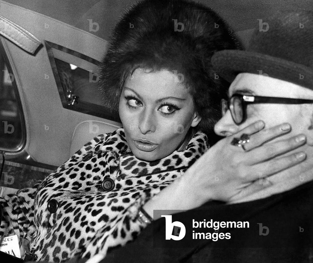 Carlo Ponti film producer has his cheek stroked by Sophia Loren actress and wife to be in back of limousine, 16th January 1966 (b/w photo)