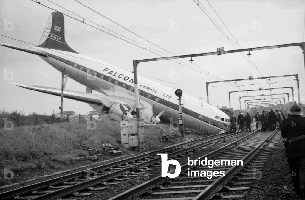 The wreckage of a fully-laden passenger Viscount aeroplane after it had overshot the runway at Rochford Airport and ended tail up on the railway line which runs alongside the airport. 
Firemen and emergency services clear the way for passengers to exit the plane.
October 1960