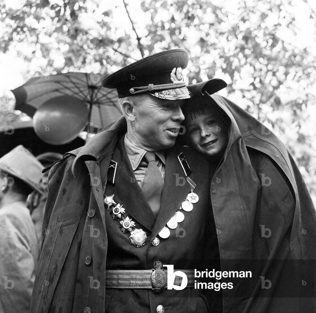 A soldier shelters his son from the rain under his greycoat during the May Day celebratins in Tbilisi, Georgia, USSR. May 1960
