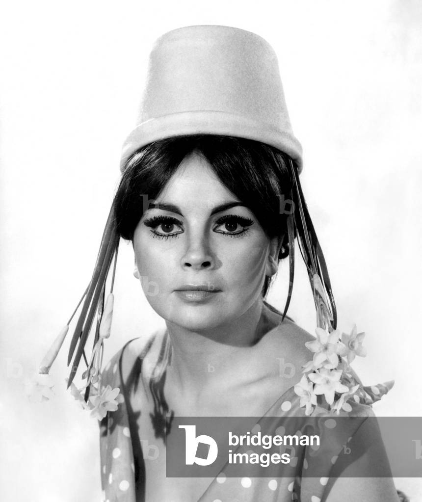 Daffy-Down-Dilly. Woman wearing a n unusual hat in the form of an upside down plnat pot with the flowers making her hair longer
March 1967