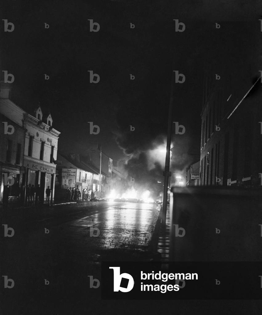 Northern Ireland Belfast Falls Road August 1969. Policeman standing with machine gun; and petrol bombs exploding round armoured car with RUC men in background. August 1969 Z8047-004