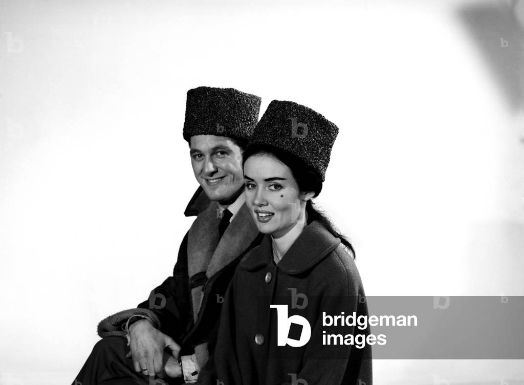 Clothing: Fashion: Hats: Man and woman wearing cossack hats. Models: Barbara Turner and Mike Lester, January 1963 (b/w photo)