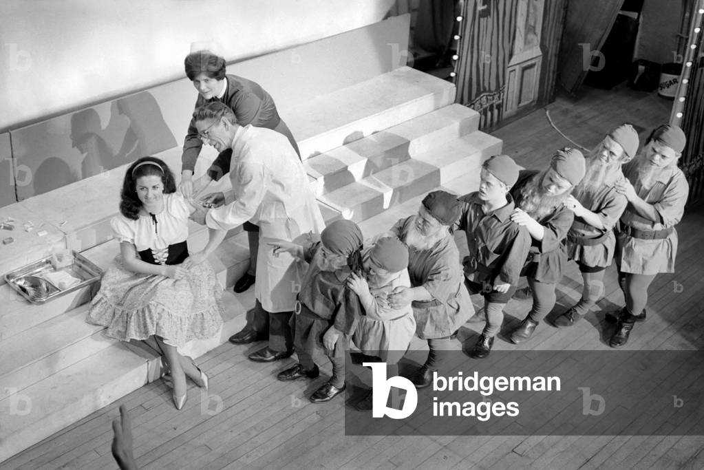 A doctor with his syringe makes ready to give anti-flu vaccine to Margaret Ayre, who plays Snow White and the rest of the cast at the City Varieties, Leeds. December 1969