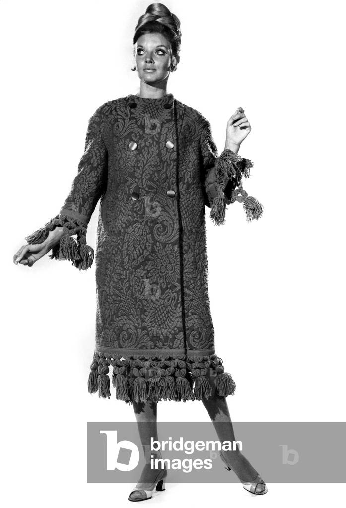 Reveille Fashions: Maureen Walker. Be original, wrap up warmly in your bedspread. Our coat is in blue and green heavy tapestry cotton, trimmed at the cuffs, hem and round the hood with a green fringe, October 1968 (b/w photo)