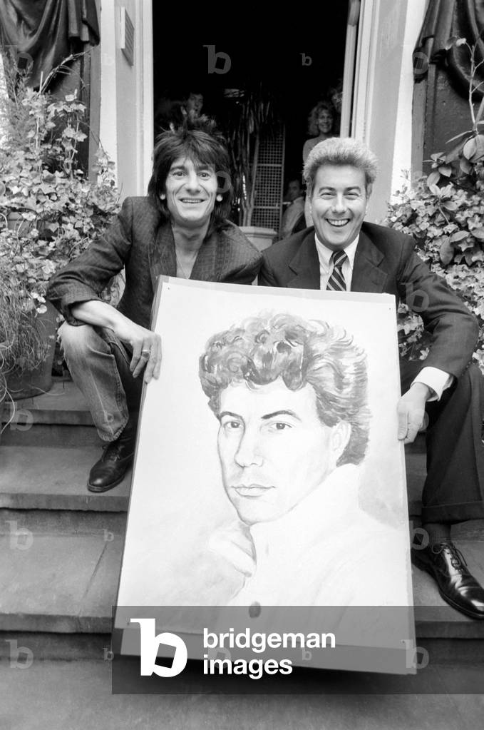 Rolling Stones: Ronnie Wood holds a painting of author Ken Follett who stands next to him. September 1987