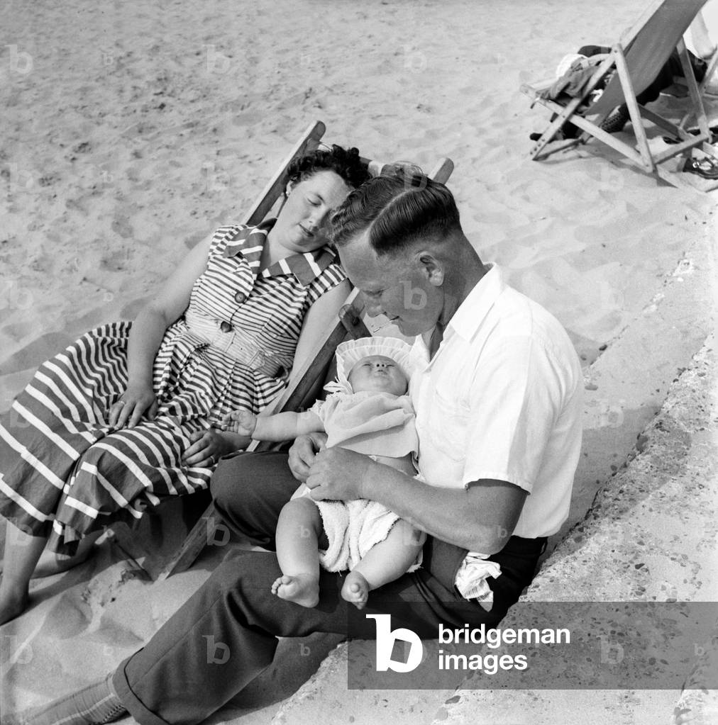 Now there is a good father. While Mummy Mrs. Toyea Brett sleeps father Mr. Paddy Brett changes the nappy on his 6 months old daughter Mandy on a day out a t the beach. June 1960
