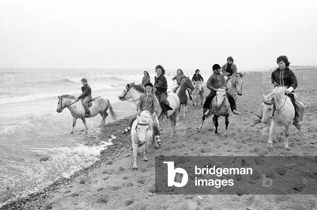 Children enjoying a seaside canter on the ponies despite the weather at Hornsea, East Riding of Yorkshire. 8th August 1977 (b/w photo)