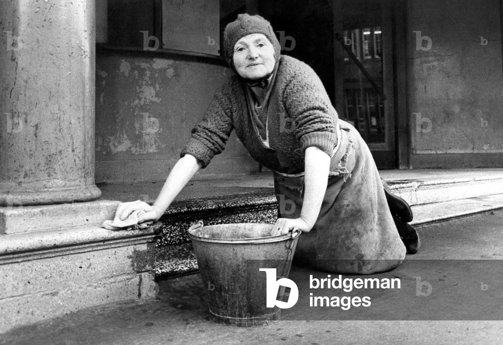 Mrs. Bella Pyle cleaning the steps at Stanley's Pavilion Cinema which has been empty for the past six years. For a couple of hours each week Bella religously scrubs the marble steps leading to the paybox, then she dusts and polishes the foyer, c.1970