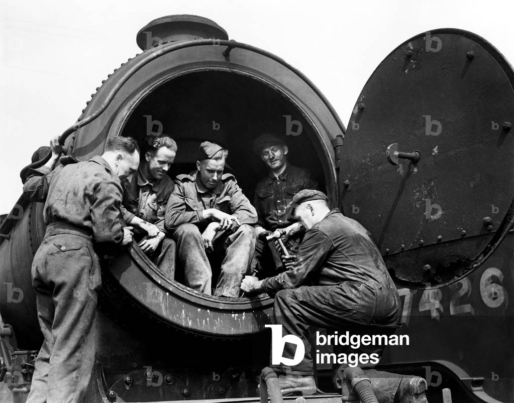 Seated comfortably in the presumably cold smokebox, army trainees watch their instructor remove scale from an LNER Thomson class B1 loco, 18th July 1944 (b/w photo)