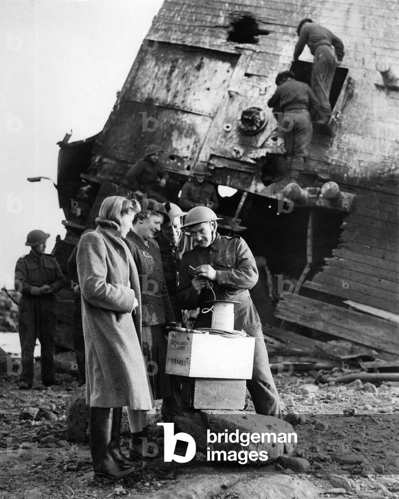 A soldier talking with women at a salvage yard. 
December 1942