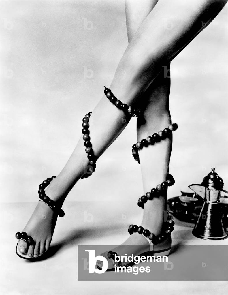 Woman wearing unusual pair of shoes with beads wrapped around her legs. 
July 1969