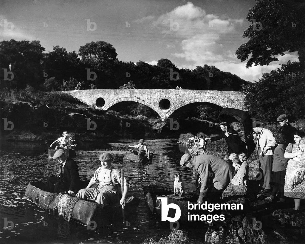 By the famous Cenarth bridge the coracle fishers set out for a day's fishing. They work in pairs and each pair must keep at least 200 feet away from another. Often the womenfolk and children come to see them off - wish them good catches, c. 1945 (b/w photo)