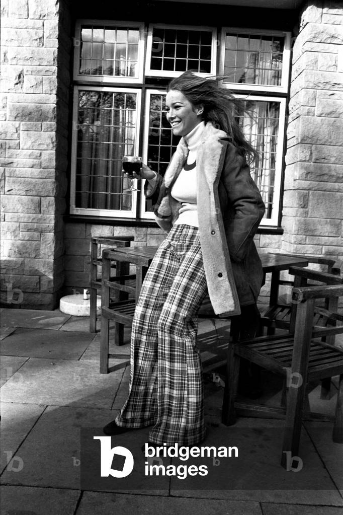 A model wearing a winter coat and tartan trousers during a fashion shoot, 26th October 1971 (b/w photo)