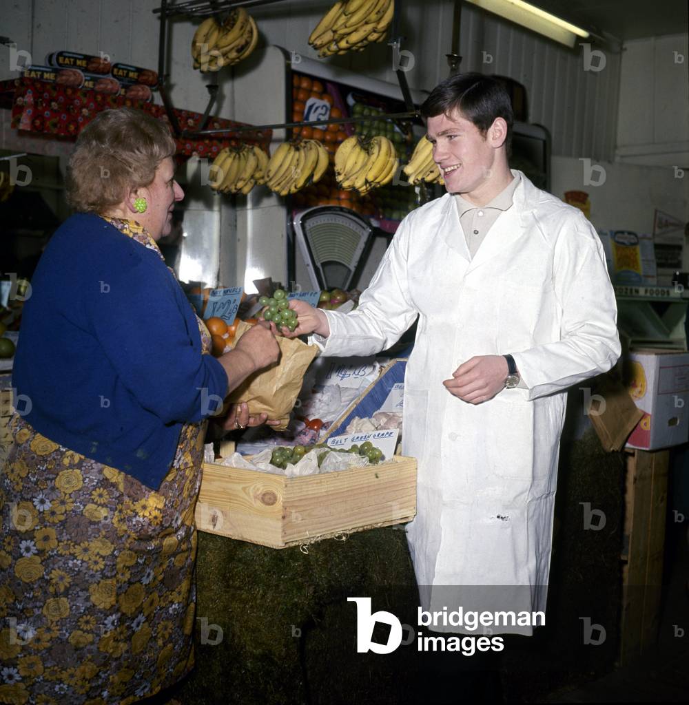 Arsenal footballer Pat Rice serves a customer while working on his London fruit stallFebruary 1968 (photo)