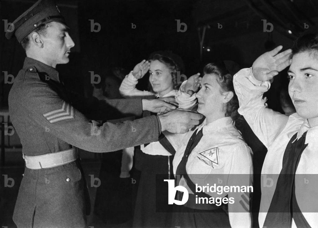 Sargeant Shorter of the Coldstream Guards instructing the new recruits of the girls training Corp at Chelsea. 
Every Sunday he gives his own time to help in training these girls who will become technicians, nurses etc.  
One girlgis corrected after making a saluting mistake. January 1942