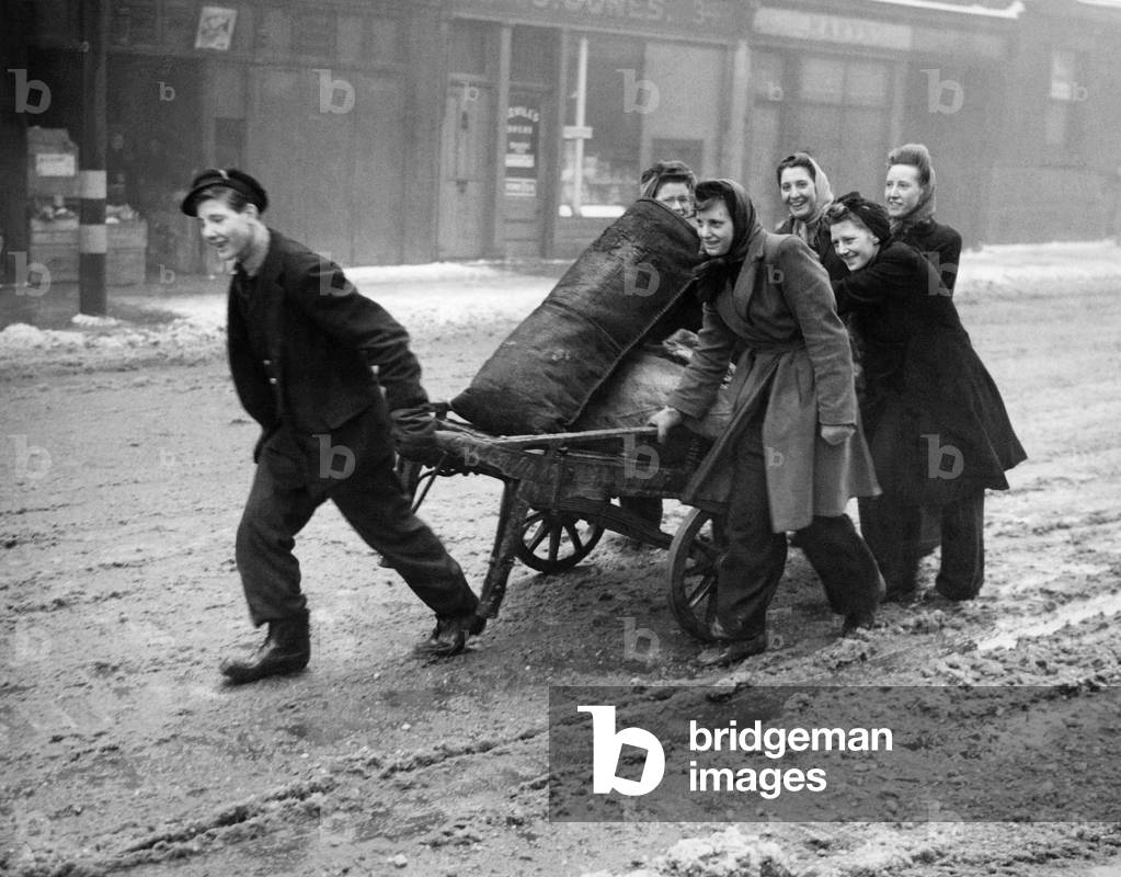 Coal shortage - a scene in sloshy Caledonian Road, London, as women assist a worker to get the coal home. January 1945