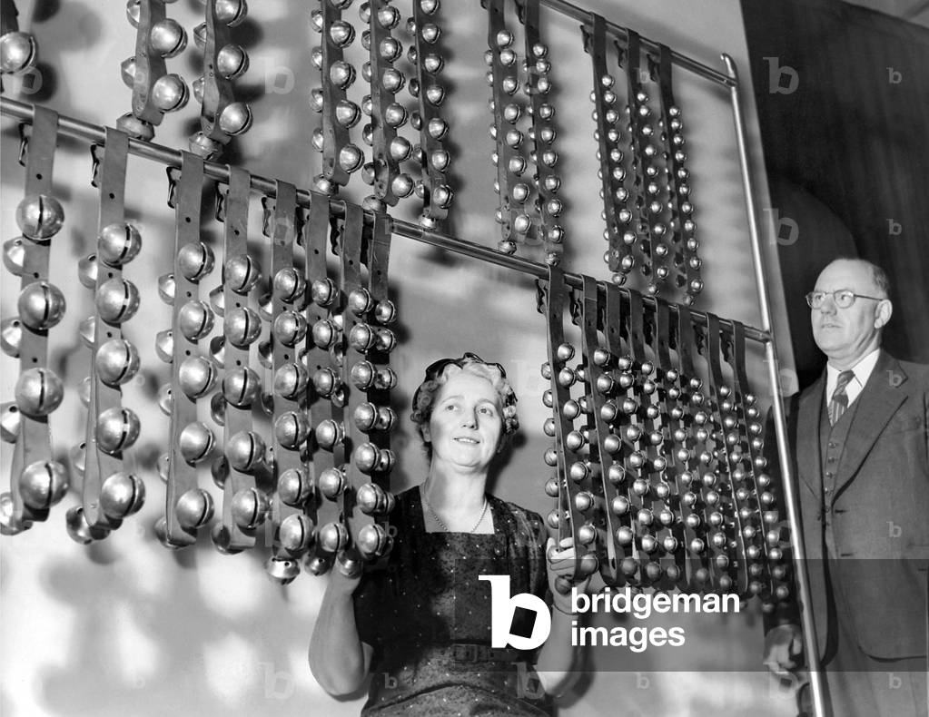 Mrs. Ritchie operates the 424 sleigh bells while her husband looks on in April 1960 (b/w photo)