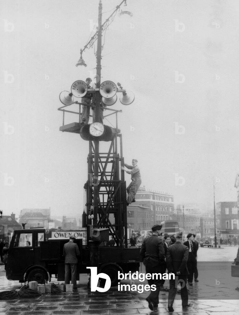 Workmen are erecting the scaffolding for the loud speakers in readiness for the Prime Minister's speech on VE Day in Broadgate, Coventry. We can see the time on the clock is 10, 20 am, 8th May 1945 (b/w photo)