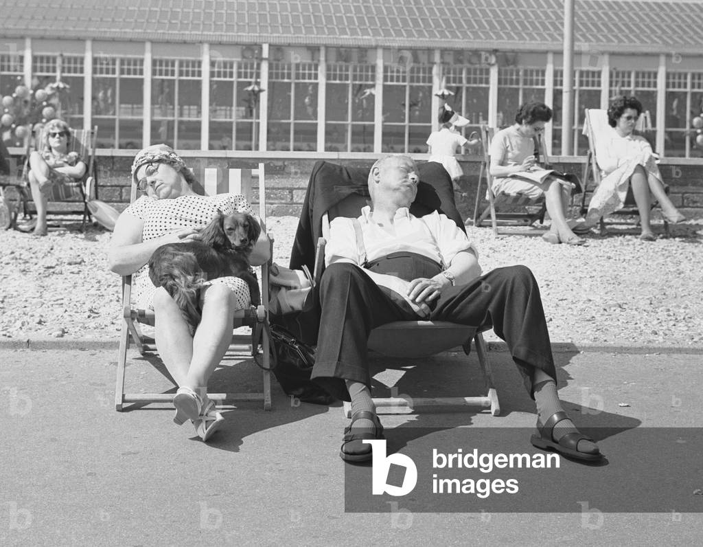 Seaside Holiday - Butlins of Bognor. A couple sleeping in their deckchairs with their dog on the promenade at Bognor Regis 10th June 1962 (b/w photo)