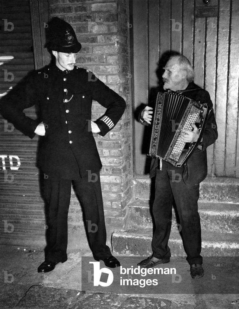 Buskers: The policeman recognizes Gus Andrews, and pauses during his beat to listen to a tune. October 1947 P018612