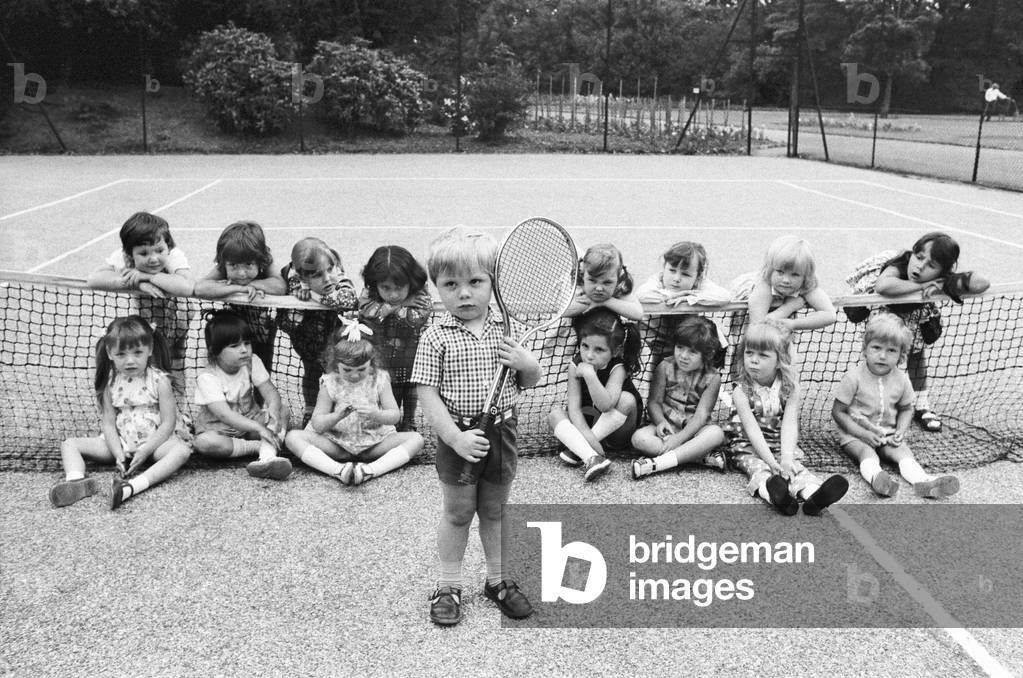 Three year old Daniel Jarmin holds a tennis racket as he poses with other friends in his class at a kindergarten school he attends in Ilford, Greater London. Daniel is a possible Wimbledon entry of the future. 19th June 1973 (b/w photo)