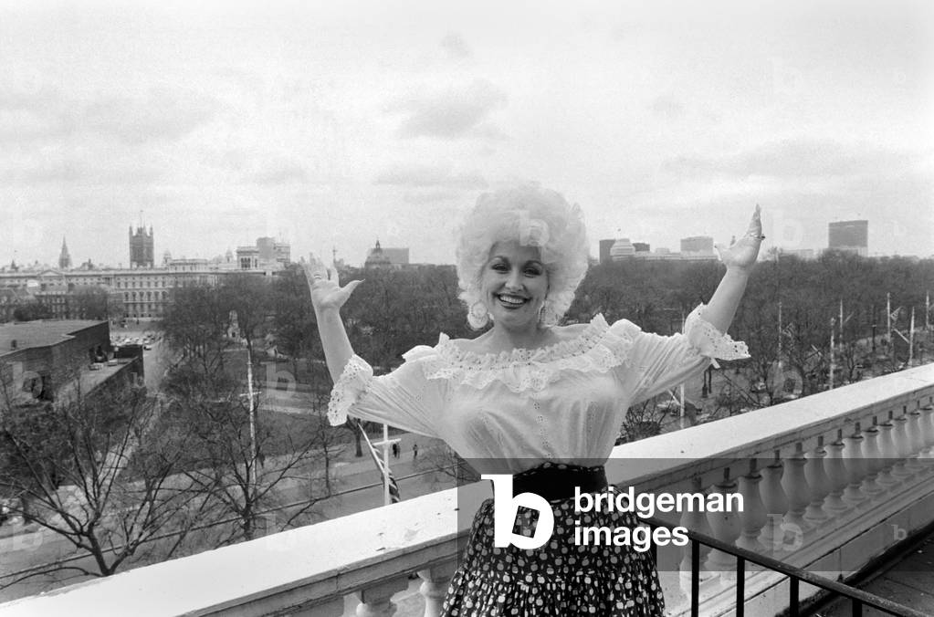 Dolly Comes To Town. American Country and Western singer and film star Dolly Parton, on top of the world, as she has her first look at London, on the roof of the Dorchester hotel, 24th March 1983 (b/w photo)