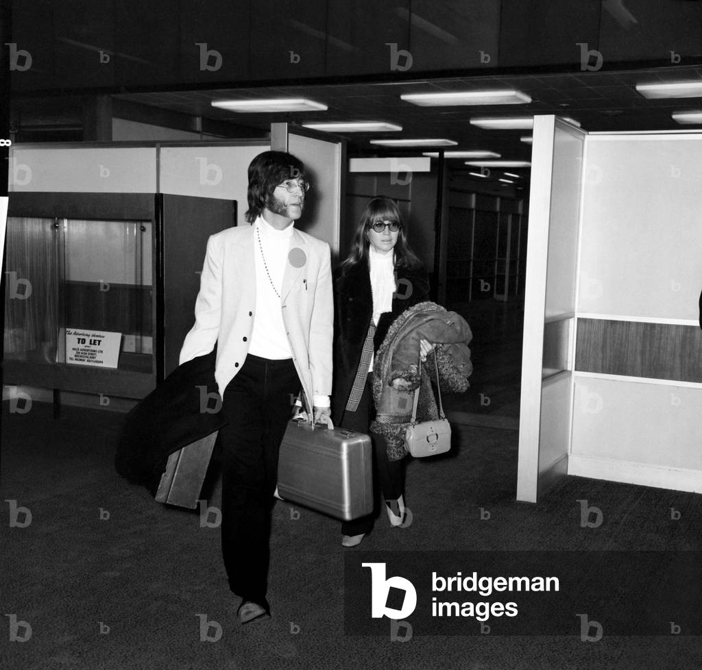 John Lennon and his wife Cynthia wearing trouser suit, beret and glasses in the airport, 15th February 1968 (b/w photo)