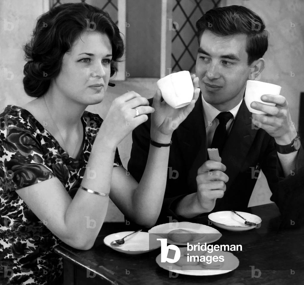 Young couple enjoying cups of tea and biscuits whilst flirting with each other, 21/09/1960 (b/w photo)