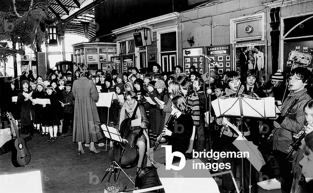 These schoolchildren get into the festive mood carol singng at a Tyneside railway station in 1979 (b/w photo)