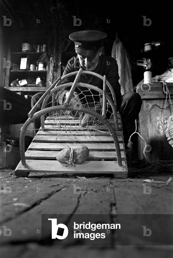 Industry: Fishing: An old fisherman of Beadnell on the Northumberland coast, fixing lobster pots in his hut. November 1969