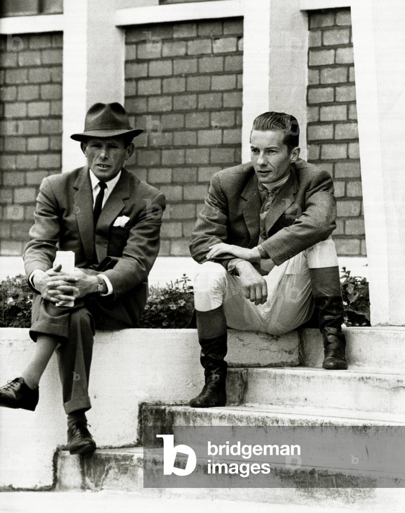 Lester Piggott sits outside the weighing-in room, chatting with friends, before the fifth race July 1962 (b/w photo)