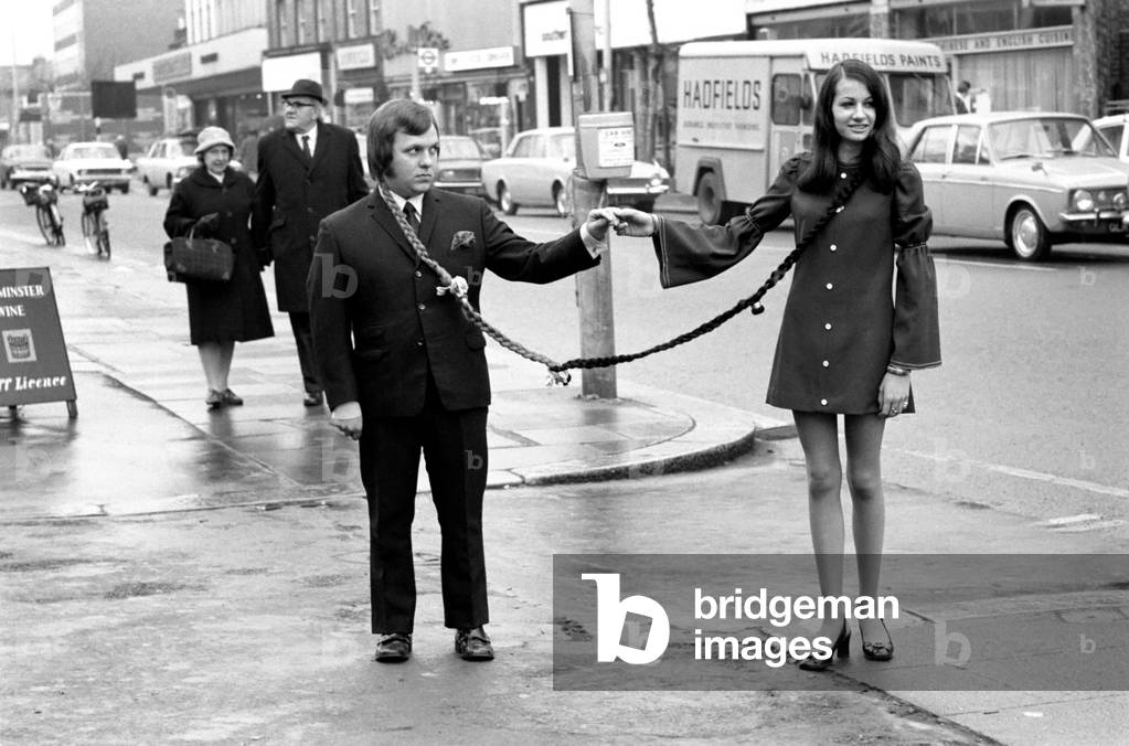 Ian Newman (19) a car salesman in Hounslow was getting worried as every time he got a new girlfriend and took her to dances other men who took a fancy to his girl would steal off with her and so Ian was left girl-less. But now he has the solution provided for him by hairdresser Len Pountney who has designed a long pigtail from Ian's hair that connects to Gloria Wootton (15) a florist, so that now everywhere the couple goes they are linked together. Ian Newman and Gloria Wootton linked in the high street today. November 1969