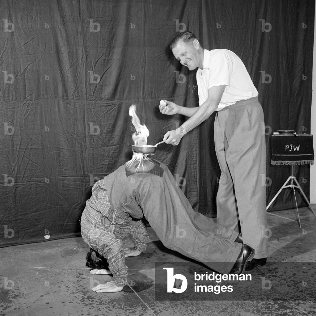 In The Hot Seat: Frank Batson fries an egg on the backside of Neville Wood to demonstrate the fireproof properties of asbestoes.
c.1955