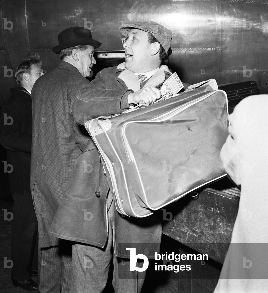 Managing director of British United Airways Freddie Laker, loads luggage onto an aircraft at Gatwick airport during a strike by porters. 
1st December 1964.