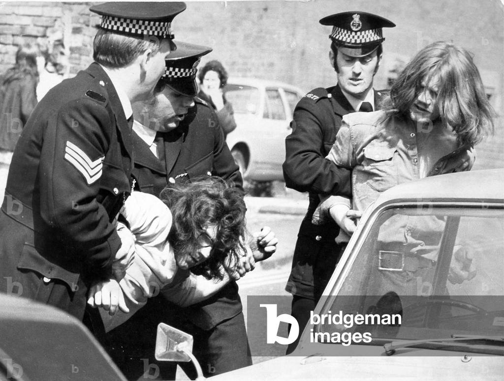A young man is arrested by police after a disturbance and bundled into a waiting police car, c.1970