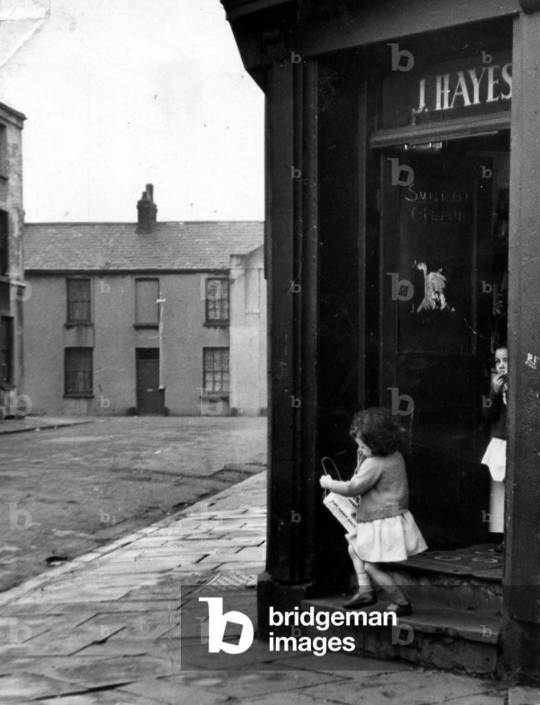Cardiff - Old - A young child leaves a typical Cardiff corner shop in Butetown. Sign on the door says 'Sunday Opening', 12th February 1960 (b/w photo)