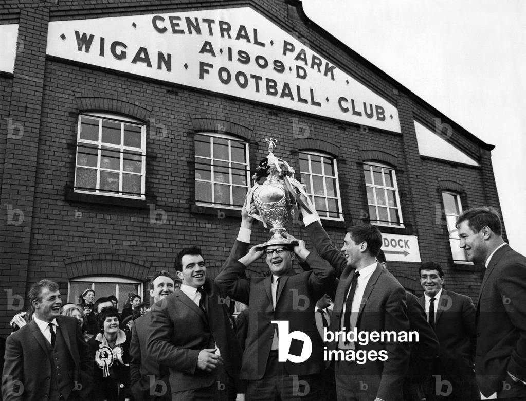 Wigan Rugby F.C. return. The triumphant Wigan Rugby Team parade outside their ground at Central Park Wigan, and clown of the team, Danny Gardener tries it on the size. May 1965