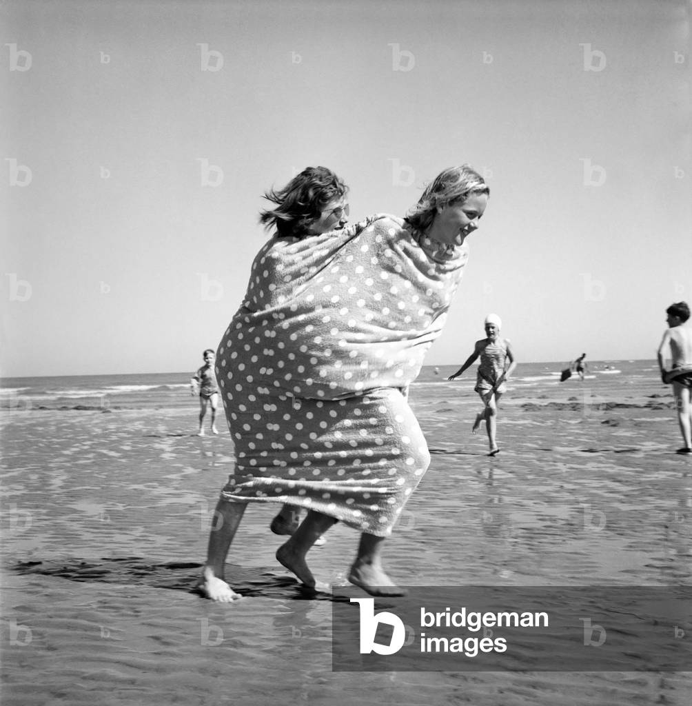 Two girls wrapped in a tent towel on the beach.