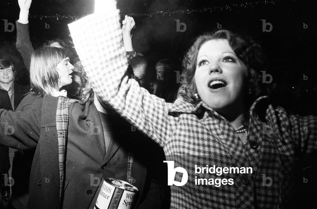 A happy crowd of young people greet the New Year in high-spirits in Broadgate, Coventry. But for one couple it's a much more personal occasion. 1st January 1973 (b/w photo)
