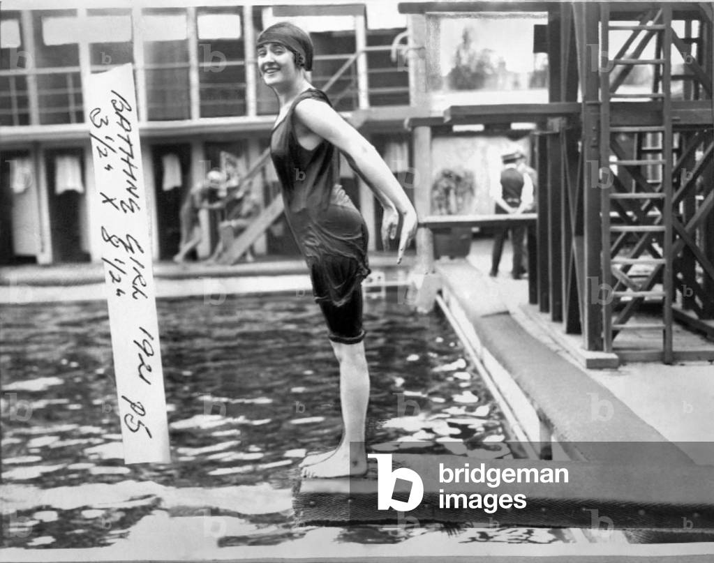 Woman in a 1920's style swimming costume about to dive in to a swimming pool, durng a heatwave.