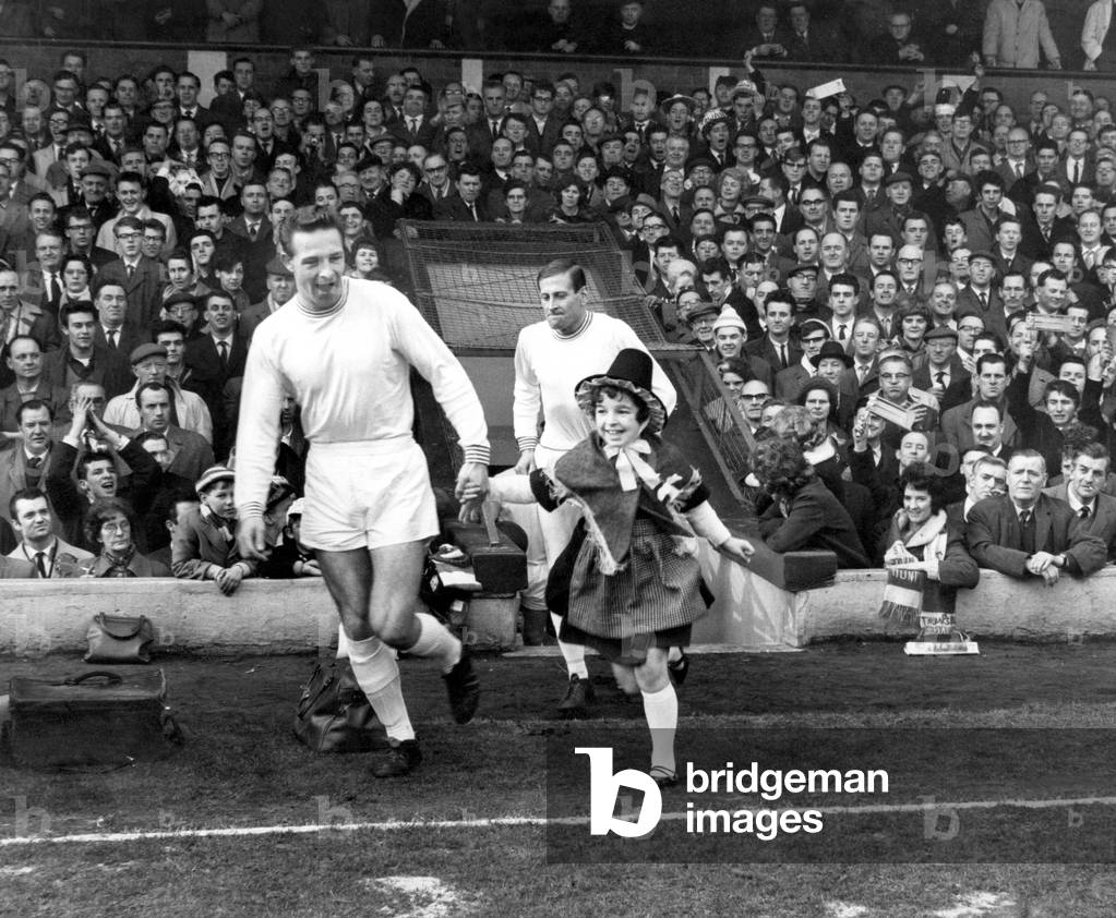 Sport - Football - Swansea Town - Swans full back and captain Brian Hughes is accompanied by young mascot Denise Peyton as the team takes the field at Anfield for their FA Cup Quarter Final tie v Liverpool. The Swans won the tie 2-1 - 29th February 1964 (photo)