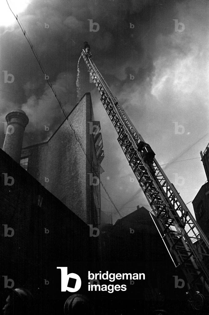 Firefighter tackle a fire following the V1 bombing of Brown Brothers in Great Eastern Street, July 1944 (b/w photo)