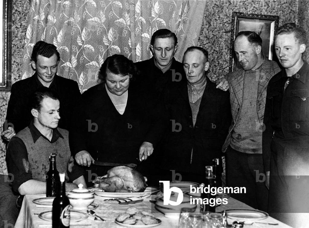 Miss Eleanor Vallans, of Robs Haugh Farm near Ponteland, Northumberland, carves a Christmas turkey for five German POWs. Her brother, Charles is second from the right. 27/12/1946 (b/w photo)
