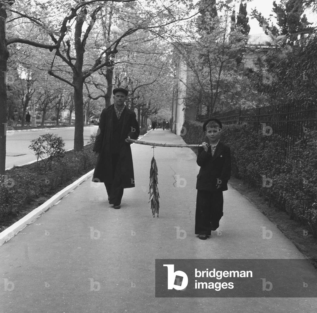 Father and son seen here walking through the streets of Moscow carrying their daily catch from the Moskva River. 25th May 1960 (b/w photo)