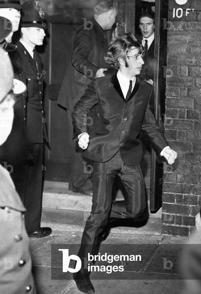 Beatles drummer Ringo Starr bolts from a side exit to a waiting car after the band's performance at the Empire Theatre in Liverpool. 7th December 1963 (b/w photo)